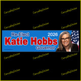 Bumper Sticker or Magnetic Bumper Sticker says, Re-Elect Katie Hobbs Governor 2026. Features photo of Hobbs with U.S. flag on a blue background.