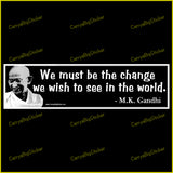 Bumper Sticker or Magnetic Bumper Sticker says, We Must be the change we wish to see in the world. Quote is credited to M.K. Gandhi. White lettering on black background with photo of Gandhi.